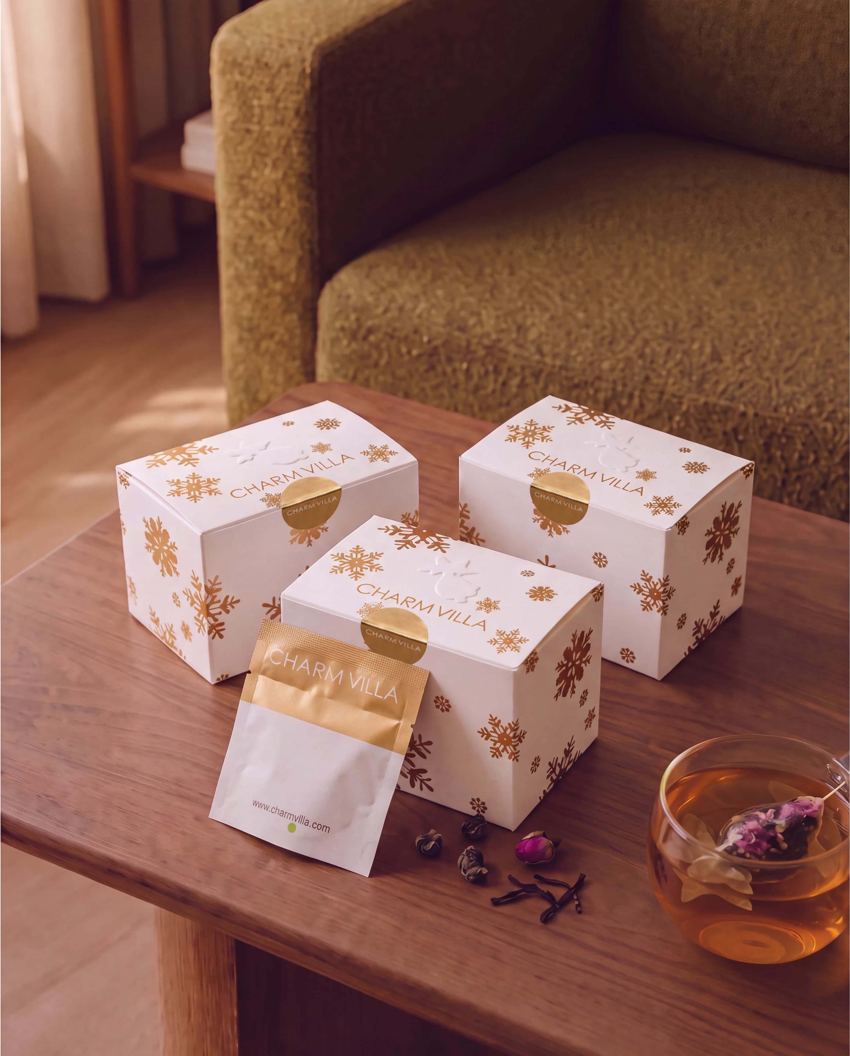 Three Christmas Charming Gift boxes on a walnut side table, with a tea pouch and a cup of goldfish tea